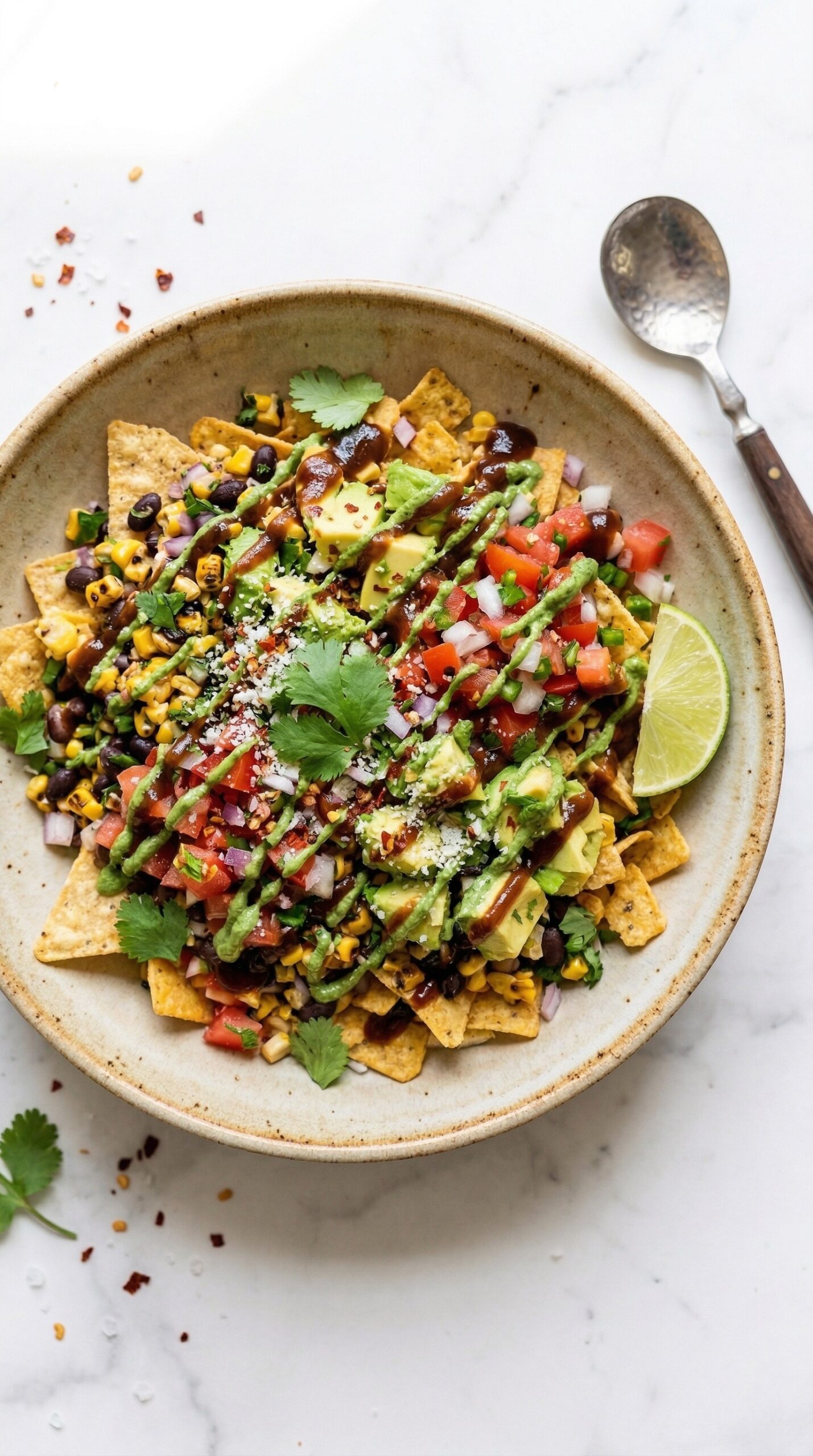 Mexican bhel in a wide shallow bowl with tortilla chips, bean and corn salsa, avocado chunks, tamarind chutney drizzle, and fresh cilantro on white marble